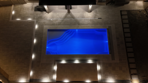 An aerial view of a custom in-ground pool with vibrant blue lighting and a surrounding patio at night by Sun Leisure Pools & Spas in Sparks, NV.
