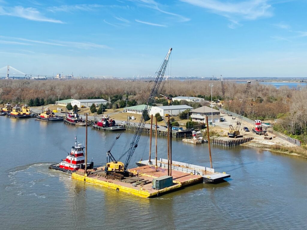 An aerial view of a tugboat from Myrick Marine Contracting Corp. in Norfolk, VA, towing a crane barge on the river.