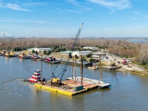 An aerial view of a tugboat from Myrick Marine Contracting Corp. in Norfolk, VA, towing a crane barge on the river.