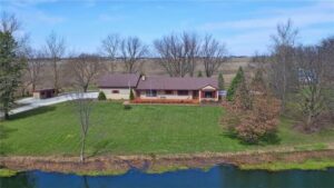 An aerial view of a beautiful, well-maintained residential property with a large green lawn and pond, serviced by Nice & Precise Lawn Care in Ames, IA.