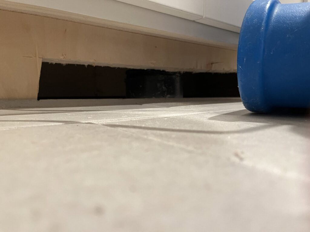 An air mover positioned to dry under a kitchen cabinet kick plate, demonstrating thorough water damage drying by Cowboy Certified Plumbing & Water Cleanup in Lee's Summit, MO.