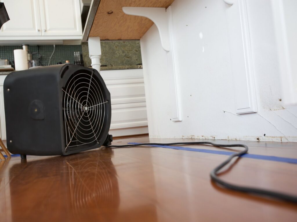 A black air mover fan drying a wooden kitchen floor after water damage, provided by A1 Restoration of Spokane in Post Falls, ID.