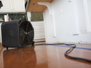 A black air mover fan drying a wooden kitchen floor after water damage, provided by A1 Restoration of Spokane in Post Falls, ID.