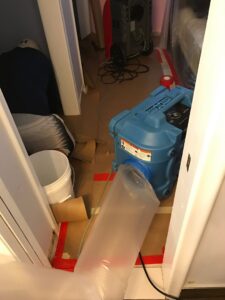 An air mover with a flexible duct and red tape on the floor, indicating water damage drying in progress by Southcoast Cleaning Solutions & Restoration in Fall River, MA.