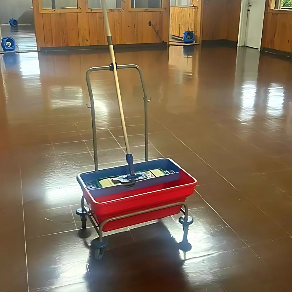A mop bucket on a wet floor with air movers in the background, indicating water damage drying by Superior Contract Cleaning in Lafayette, LA.