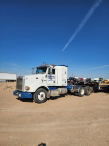 A white semi-truck with a flatbed trailer, used for heavy equipment transport by Alliance Towing and Transport LLC in Monahans, TX.