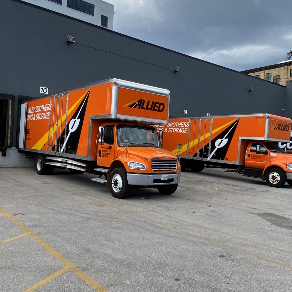 Two orange Allied moving trucks for Coakley Brothers & Brothers Interiors parked at a loading dock in Milwaukee, WI.