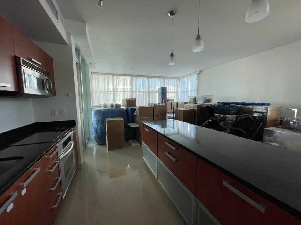 An apartment living area and kitchenette filled with packed boxes and wrapped items, ready for a move by Orellana AV Moving in Miami, FL.
