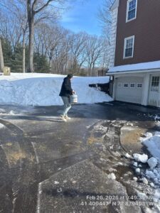 A person applying ice melt to a partially cleared driveway after snow removal by Diamond Image in New Haven, CT.