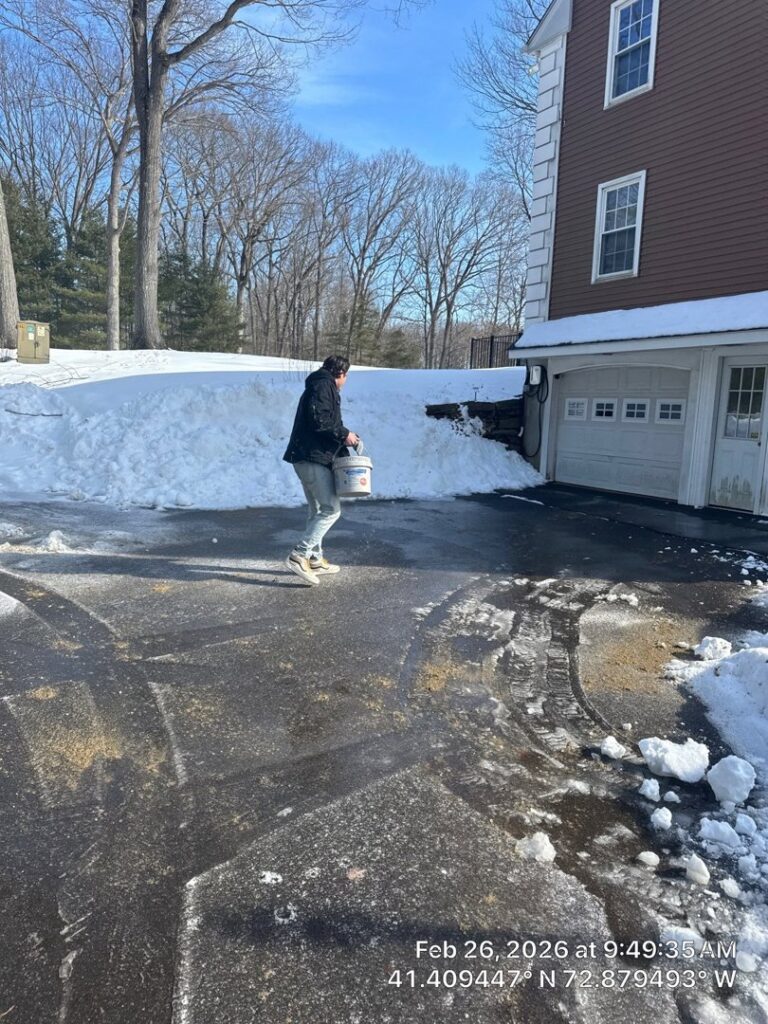 A person applying ice melt to a partially cleared driveway after snow removal by Diamond Image in New Haven, CT.