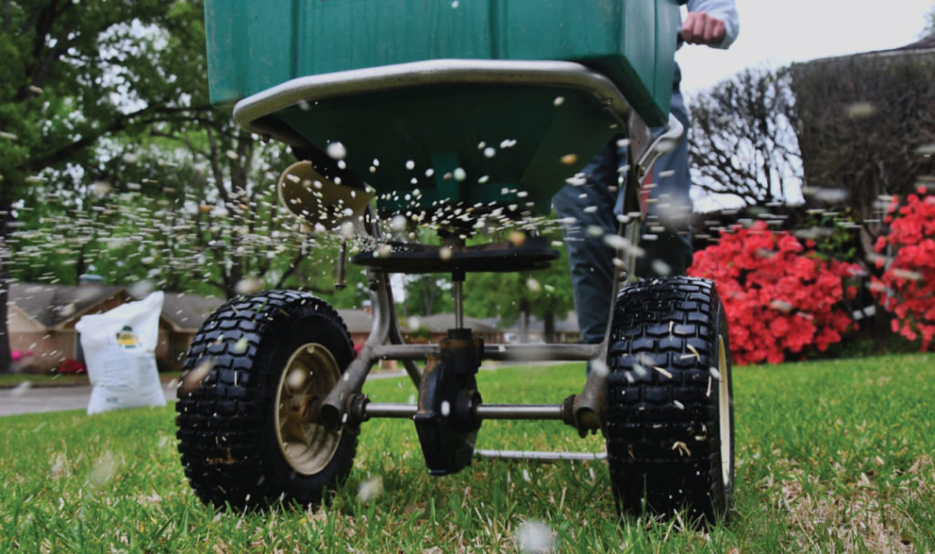 Close-up of a lawn spreader applying granular treatment to a lawn by Tee Time Lawn Care Davenport, IA.