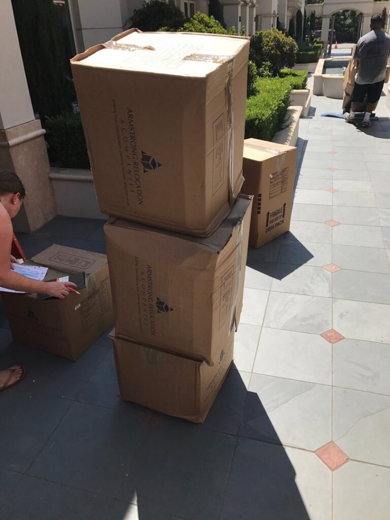 Several Armstrong Relocation branded moving boxes stacked outside a building, ready for transport by The Armstrong Company in Huntsville, AL.
