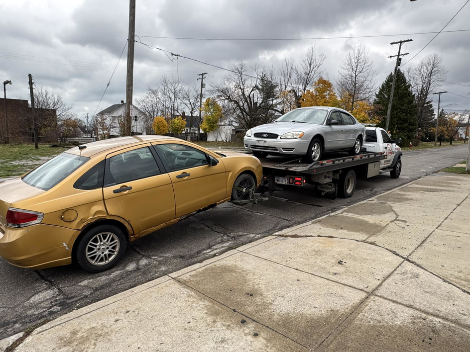 Av towing llc flatbed tow truck with a silver sedan on the bed and a gold sedan being towed by wheel lift in Cleveland, OH.