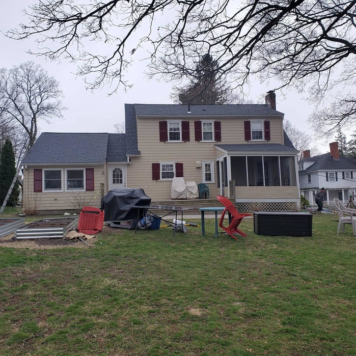 The back of a residential house featuring new yellow siding installed by Trabajo en roofing y siding in Lowell, MA.