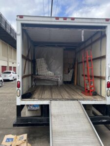 The back of a moving truck showing wrapped furniture and a hand truck inside, handled by E.L.I Movers LLC in Houston, TX.