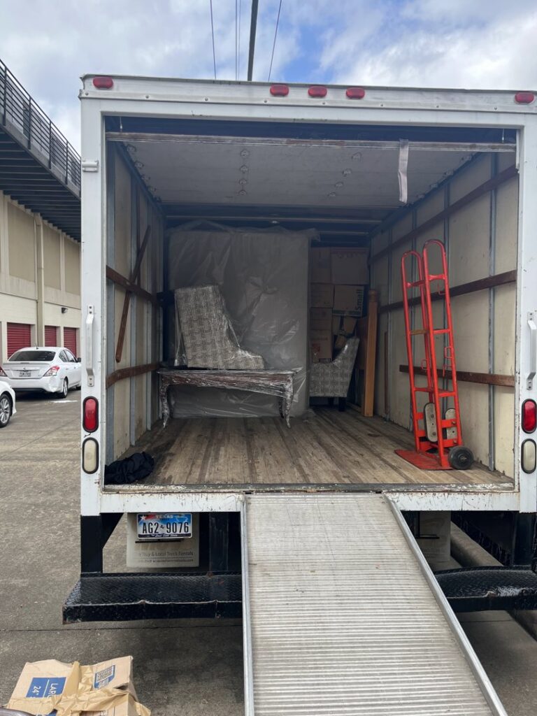 The back of a moving truck showing wrapped furniture and a hand truck inside, handled by E.L.I Movers LLC in Houston, TX.