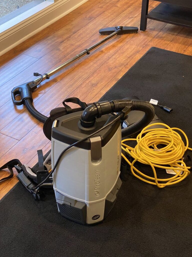 A professional backpack vacuum cleaner on a wooden floor, used by Two Maids of Hilton Head, SC.