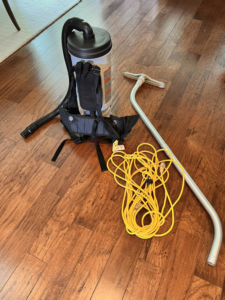 Professional backpack vacuum and cleaning tools on a hardwood floor by First Class Commercial and Residential Cleaning Services in Charlotte, NC.