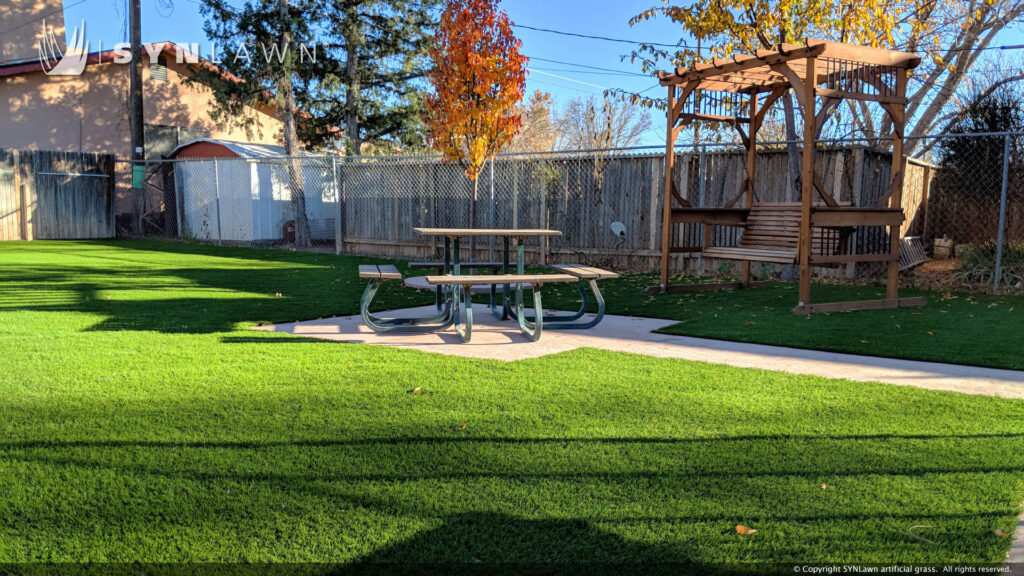 A backyard with artificial grass, a picnic table, and a wooden pergola installed by SYNLawn of New Mexico in Albuquerque, NM.