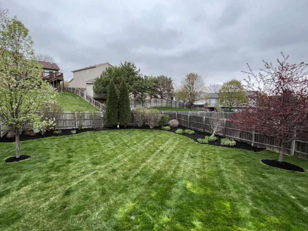 A neatly mowed backyard with fresh mulch in the garden beds, showcasing lawn care services by Kanger Lawns LLC in Omaha, NE.
