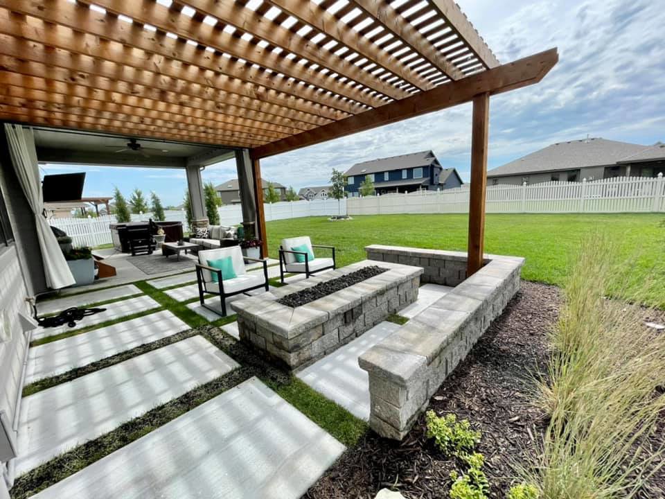 A modern backyard patio with a pergola and fire pit, featuring a lush green lawn maintained by Mitera Landscaping in Papillion, NE.
