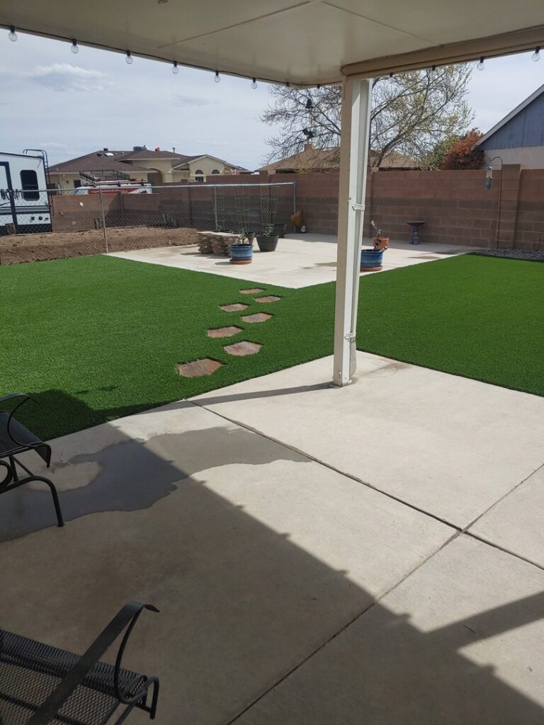 A backyard with a concrete patio, stepping stones, and artificial grass installed by SYNLawn of New Mexico in Albuquerque, NM.