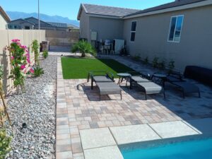 A backyard patio with pavers, artificial turf, lounge chairs, and a glimpse of a pool by Greencare.net POOL Builder in Las Vegas, NV