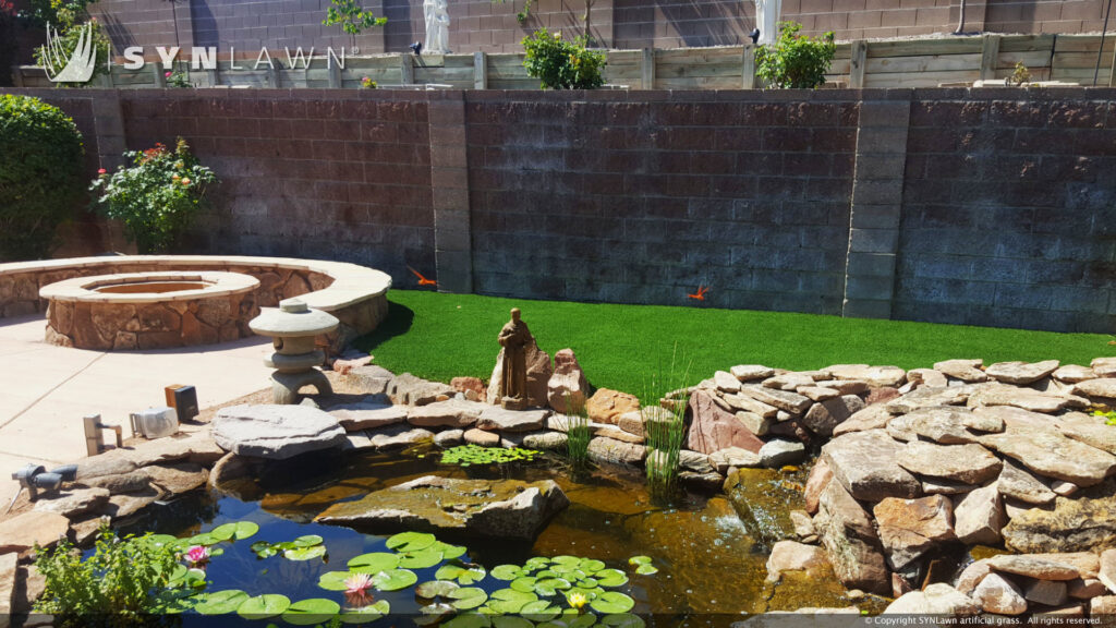 A backyard featuring a decorative pond, fire pit, and artificial grass installed by SYNLawn of New Mexico in Albuquerque, NM.