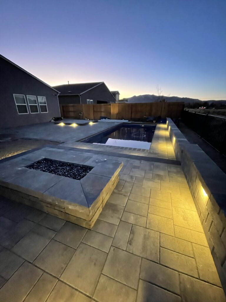 A beautifully designed backyard with a swimming pool, fire pit, and ambient lighting by Battle Born Pool & Spa in Sparks, NV.