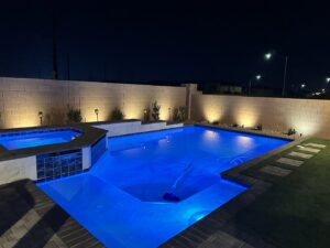 A backyard pool and spa illuminated with blue and landscape lighting at night by Greencare.net POOL Builder in Las Vegas, NV