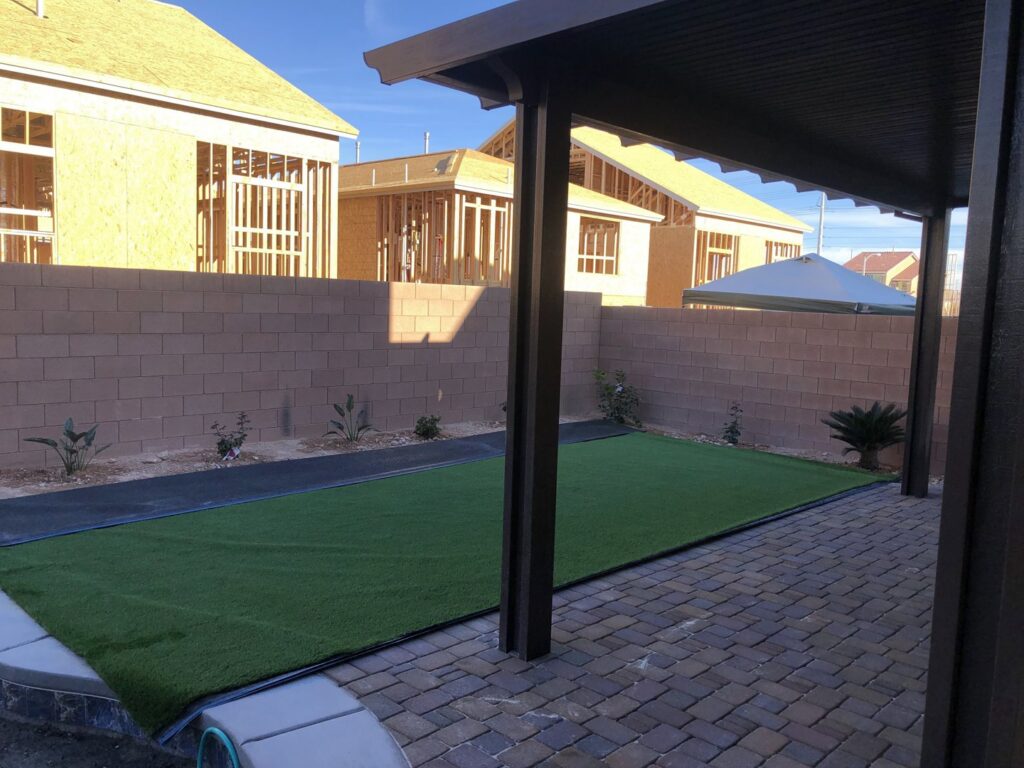 A backyard with artificial turf, pavers, and a glimpse of a pool by Greencare.net POOL Builder in Las Vegas, NV