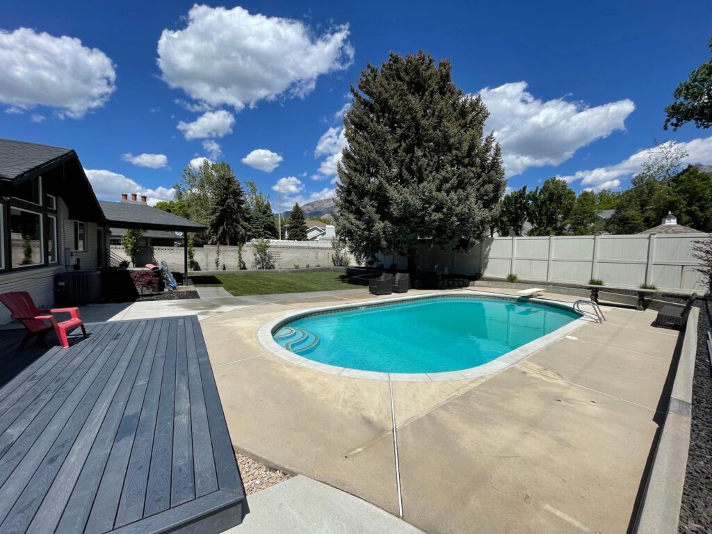 A beautiful backyard featuring a swimming pool, deck, and a well-maintained green lawn by M.D. Lawn Care & Landscaping in West Jordan, UT