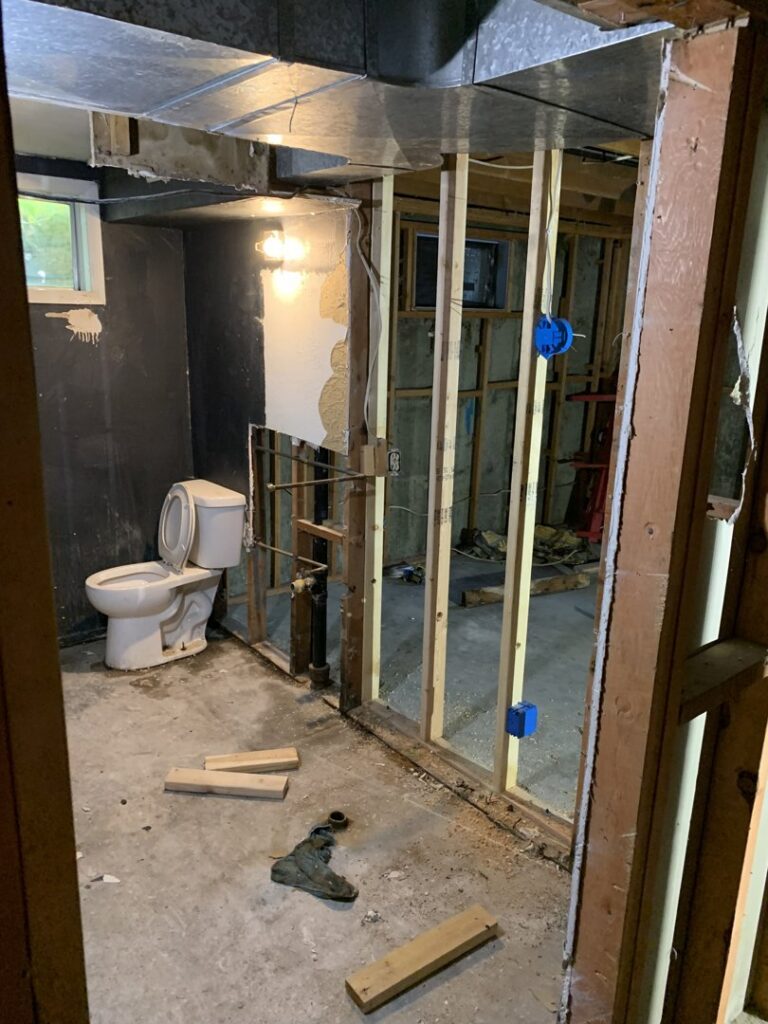 A basement bathroom undergoing demolition with exposed studs and plumbing for water damage repair by Pinnacle Paint in Casper, WY.