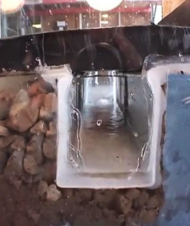 A cross-section view of a basement drainage system with water flowing, installed by Basement Doctor of West Virginia in Parkersburg, WV.