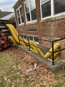 Yellow drying ducts from Clean Care of New England trailer into a basement for water damage drying in Cranston, RI