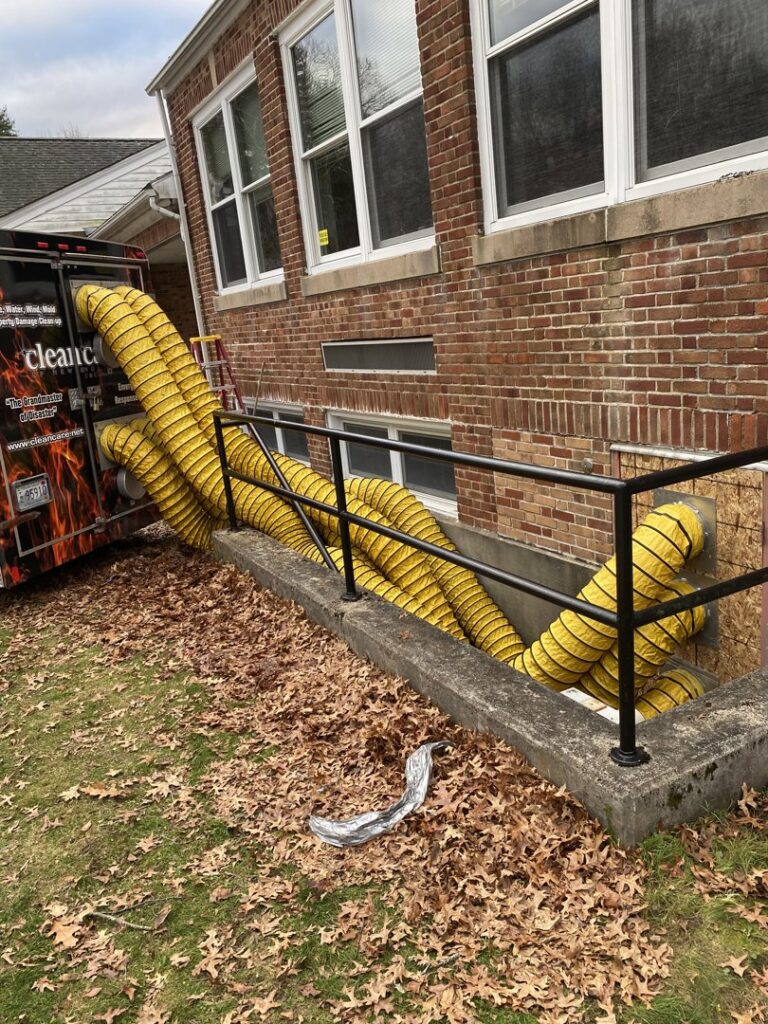 Yellow drying ducts from Clean Care of New England trailer into a basement for water damage drying in Cranston, RI