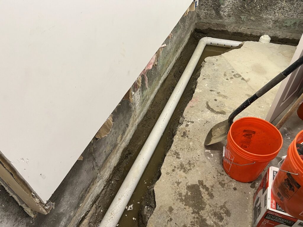 An interior basement drainage pipe being installed in a trench by EFFECTIVE WATERPROOFING in Worcester, MA.