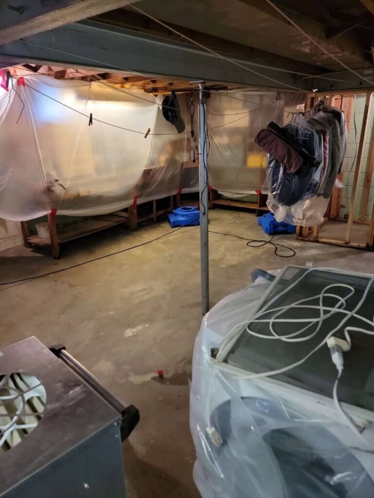 A basement with plastic containment and drying equipment set up for water damage restoration by North Shore Restore in Duluth, MN