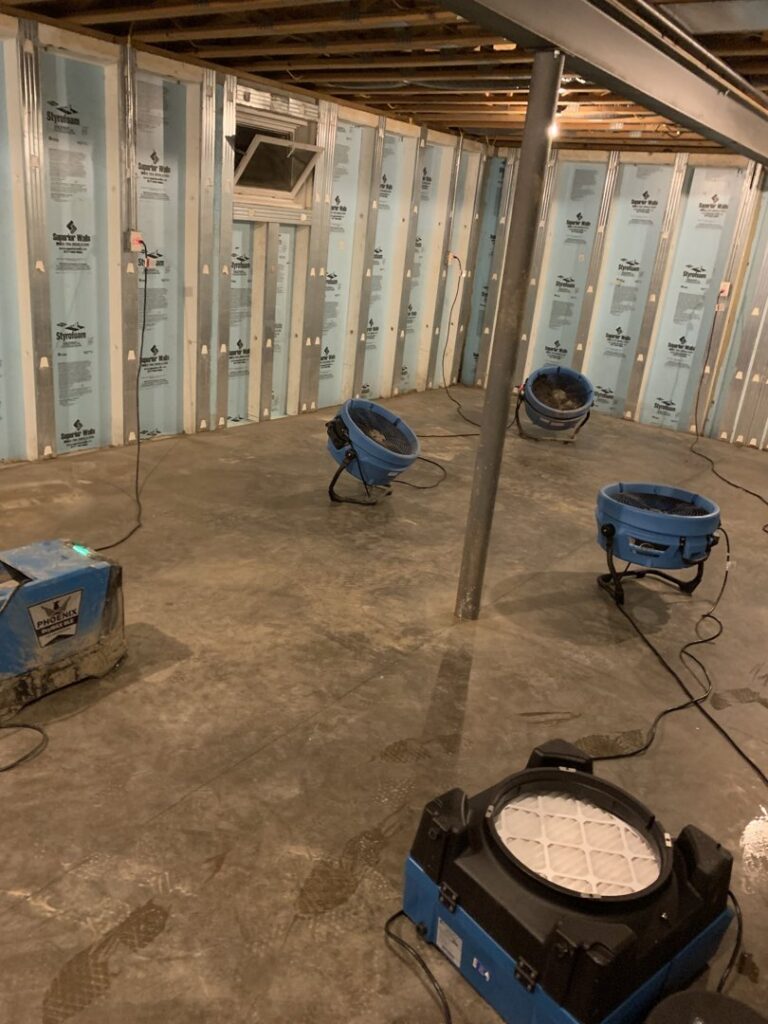 Multiple industrial air movers and dehumidifiers drying a water-damaged basement floor for Prime Restoration in Lancaster, PA.