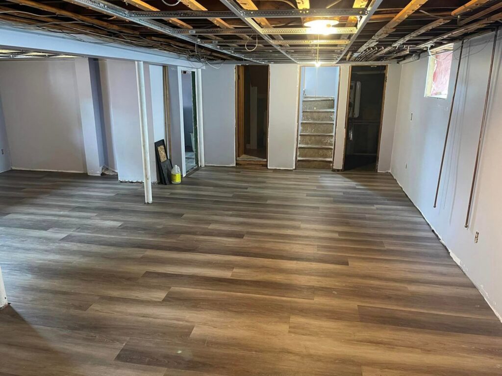 A basement undergoing water damage repair with new flooring and exposed ceiling by Mac Construction in Cranston, RI