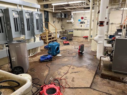 Air movers and dehumidifiers drying a wet basement floor during water damage restoration by Clean Care of New England in Cranston, RI