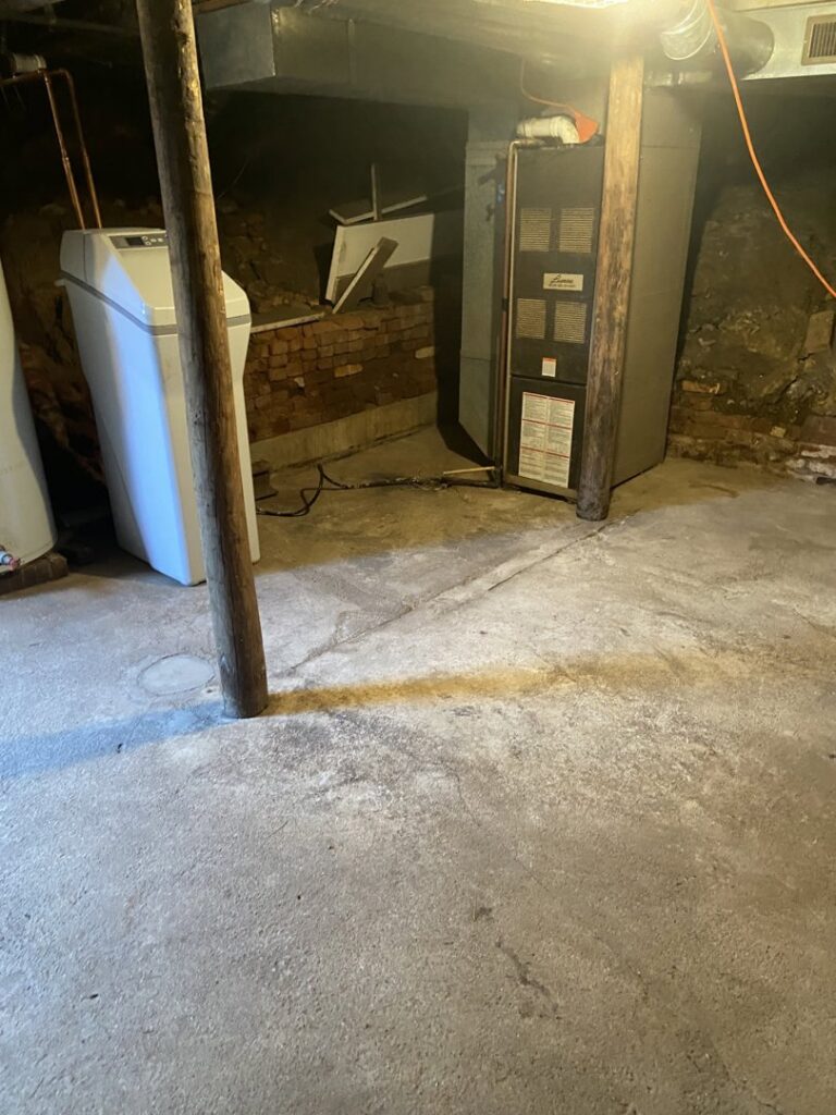 Dark water stains visible on a concrete basement floor near a water softener, indicating water damage, by Viking Restoration Services in Rochester, MN.