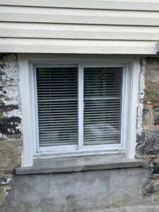 A basement window set in a stone foundation, showing potential moisture-related wear, addressed by Peach3 Group in New Rochelle, NY.