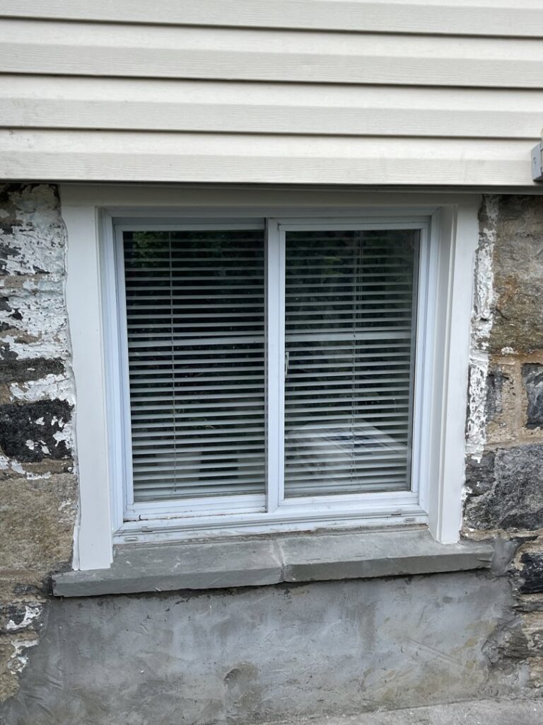 A basement window set in a stone foundation, showing potential moisture-related wear, addressed by Peach3 Group in New Rochelle, NY.