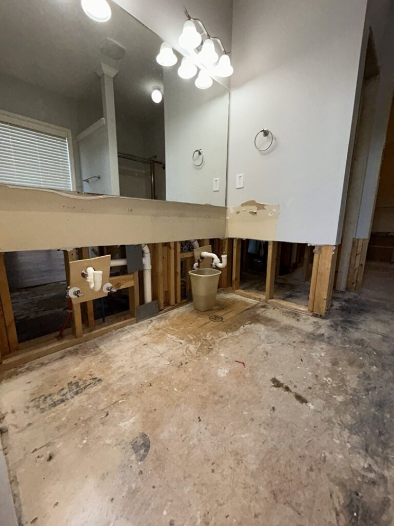 A bathroom undergoing demolition for water damage restoration, with vanity removed and exposed plumbing, by Level Creek Property Restoration in Buford, GA.
