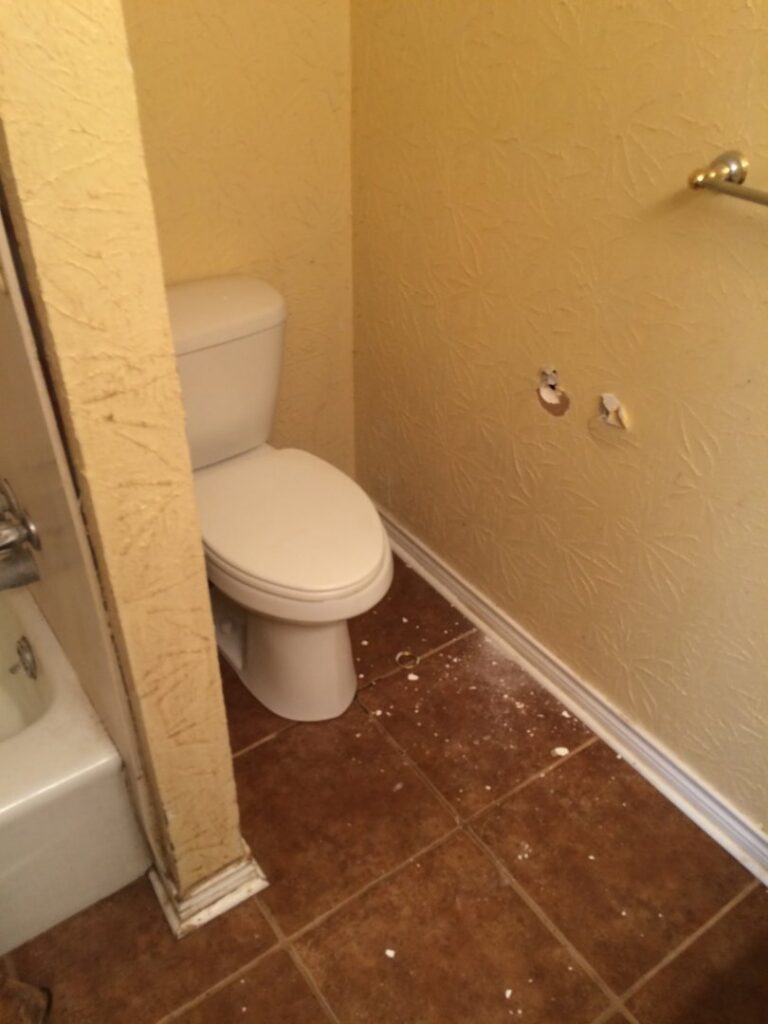 Bathroom toilet area with debris on the floor after fixture removal by Rayshawn's Home improvement & Construction work in Bossier City, LA.
