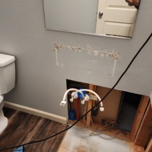 A bathroom wall with a section cut out, revealing pipes and subfloor damage for water damage repair by Verg Restoration in Vancouver, WA