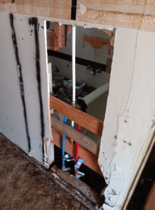 Bathroom wall demolition revealing plumbing pipes for water damage repair by Integrity Solutions in Omaha, NE.