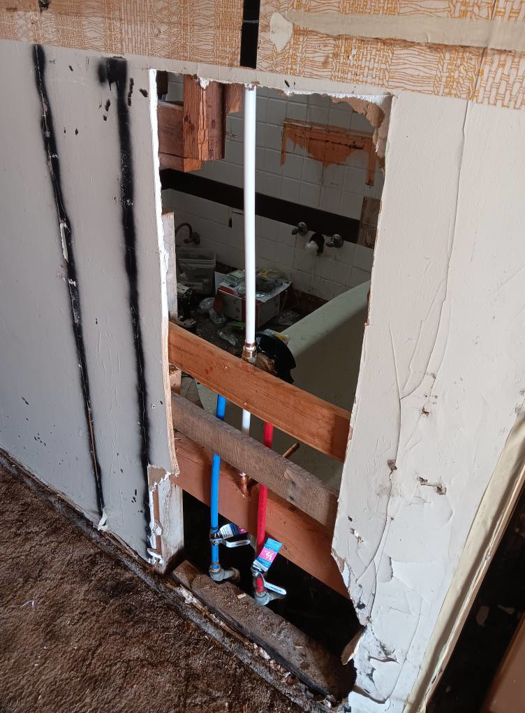 Bathroom wall demolition revealing plumbing pipes for water damage repair by Integrity Solutions in Omaha, NE.