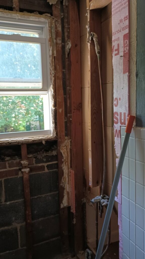 Bathroom wall with drywall removed, exposing studs and insulation, showing signs of water damage remediation by Simon Says Do It, LLC in New Castle, DE.